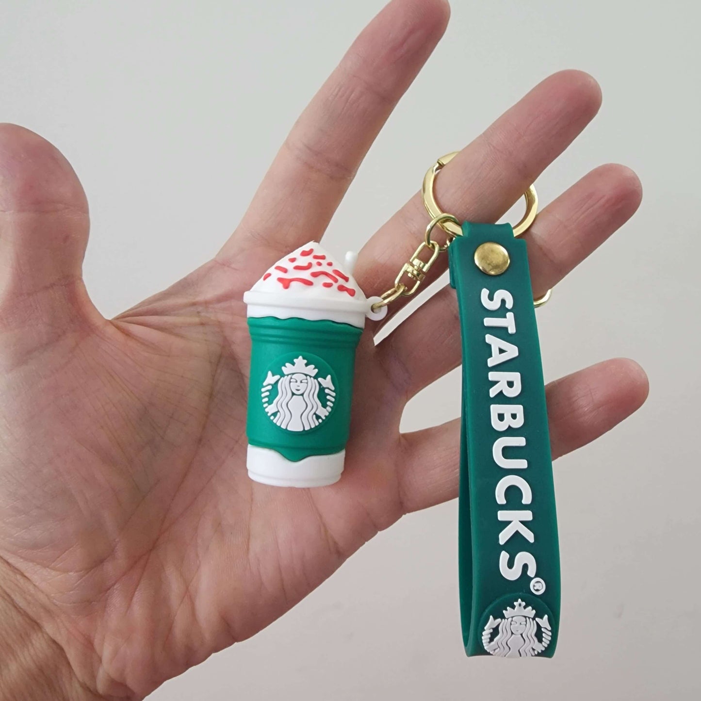 Hand holding a Starbucks key ring featuring a mini frappuccino charm with whipped cream.